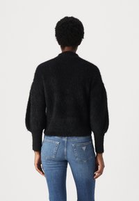 Maglione nero e fluffy a maglia con colletto alto e maniche oversize, abbinato a jeans in denim azzurro chiaro con tasche posteriori.