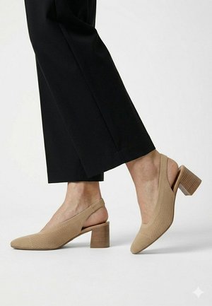 Zapatos slingback beige de tacón bajo con tejido texturizado, usados con pantalones cortos negros sobre un fondo blanco.