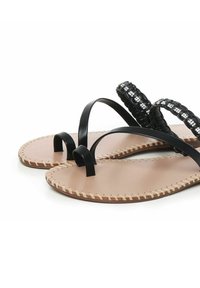 Sorte sandaler med flade såler, som har en flettet sort rem og en glat nude læderfodseng, udsmykket med stikninger langs kanten.