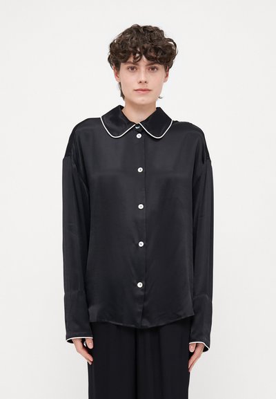 Zwarte satijnen blouse met een grote kraag, witte piping, knoopsluiting aan de voorkant en lange mouwen. Gladde textuur en oversized pasvorm.