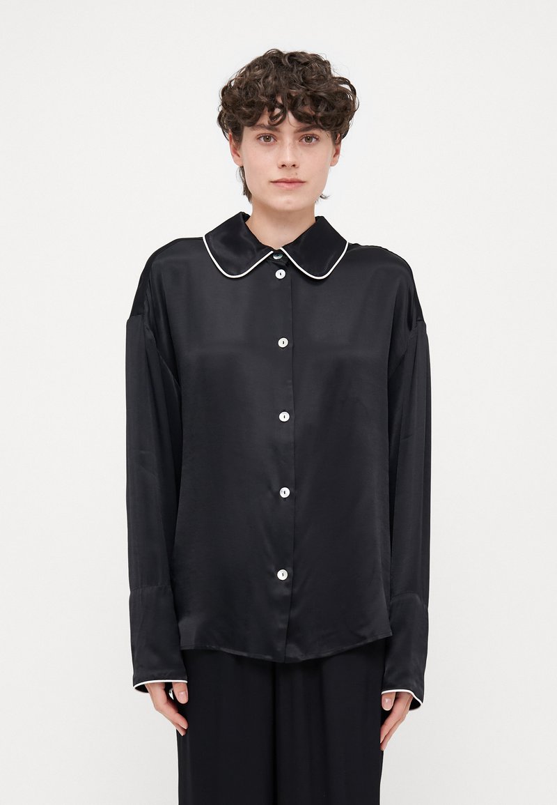 Black satin shirt with a large collar, white piping, button front, and long sleeves. Smooth texture and oversized fit.
