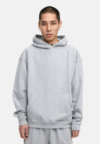 Grauer Baumwoll-Hoodie mit einer Fronttasche und einer Kapuze mit Kordelzug. Merkmale sind der lockere Schnitt, gerippte Bündchen und Saum. Leicht und mit weicher Textur.