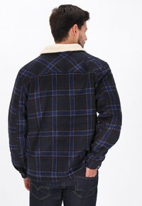 Sort ternet skjorte lavet af textureret stof, med en krave i cremefarvet faux shearling og blå og røde ternmønstre. Lange ærmer og afslappet pasform.