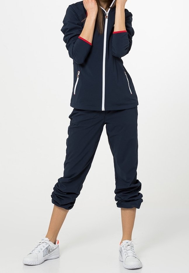 Marinblå jacka med röda detaljer och vit dragkedja, ihop med korta marinblå byxor. Båda är tillverkade av lättviktsmaterial; vita sneakers fulländar outfiten.