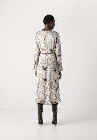 Long-sleeve dress in light fabric with a cityscape print in black and beige. Fitted waist with a black belt, paired with knee-high black boots.