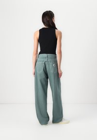 Pantaloni ampi verde chiaro con vita alta, dotati di due tasche posteriori e sottili dettagli di cucitura. Abbinati a un top senza maniche nero.