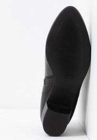 Scarpa in pelle nera con punta affusolata e una texture liscia. La suola è piatta, con un motivo a righe e una marcatura della taglia di 37.