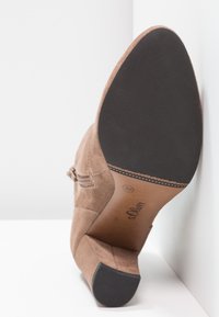 Hnědý semišový vysoký podpatek s hrotem, zakřiveným podpatkem a strukturovanou stélkou. Má hladkou černou gumovou podešev.