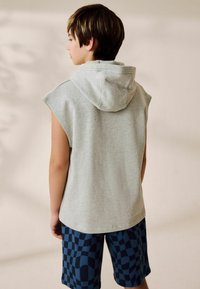 Haut sans manches gris clair avec capuche, associé à un short bleu marine à motifs avec un design en damier. Texture de tissu douce évidente.