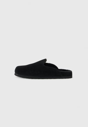 Black suede slipper with an open back, soft inner lining, and a textured rubber sole. Rounded toe and minimalistic design.