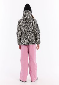 Mustavalkoinen seepra-kuosisella toppatakkilla, jossa on huppu, yhdistettynä löysiin vaaleanpunaisiin housuihin ja mustiin saapikkaisiin, kuvattu takaa.