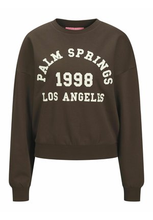 Brūns svītru krekls ar apaļu kaklu, kurā ir balts grafisks teksts "PALM SPRINGS 1998 LOS ANGELES" biezā tipogrāfijā. Elastīga josta un piedurknes.