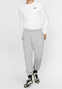 Vit långärmad skjorta med en svart Nike-logotyp; grå mjukisbyxor med en vit Nike-logotyp; svarta och gröna träningsskor med en unik design.