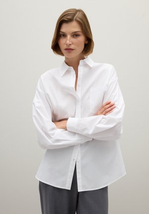 White button-up shirt made of smooth fabric, featuring a pocket on the left side, a classic collar, and long, slightly puffed sleeves.