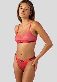 Rode lingerieset met een aansluitende bralette met dunne bandjes en bijpassende thong. Luipaardprint textuur op de thong, logo tailleband detail.