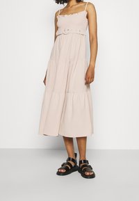 Svetle růžové šaty s volánkovými ramínky, přiléhavým živůtkem a ozdobným pásem se kulatou sponou. Nošeny s černými sandály.