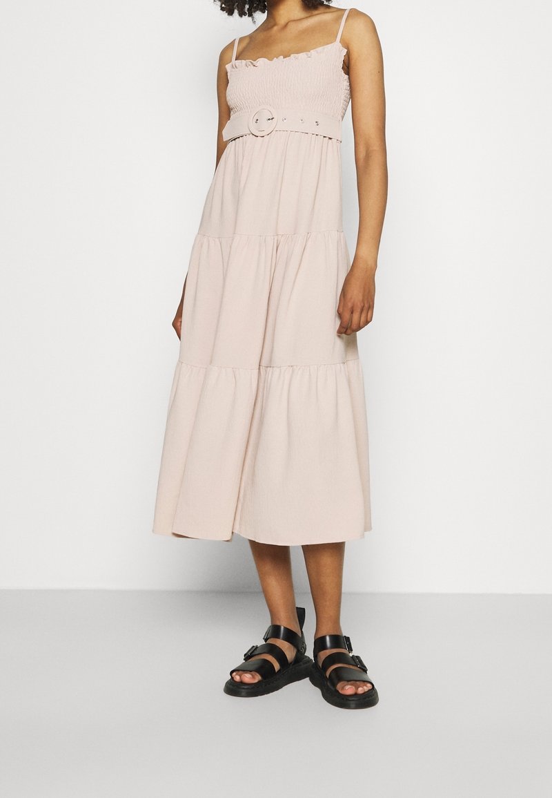 Svetle růžové šaty s volánkovými ramínky, přiléhavým živůtkem a ozdobným pásem se kulatou sponou. Nošeny s černými sandály.