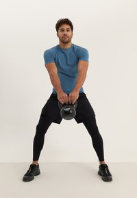 Blue athletic t-shirt with textured accents, black shorts, and black leggings. Holding a black kettlebell, wearing black training shoes.
