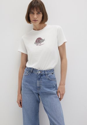 White cotton t-shirt featuring a colorful graphic of a cat with yarn. Paired with light blue high-waisted denim jeans, straight cut.