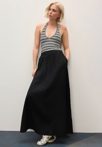 Prugasti top na halter s dubokim V-izrezom i crna duga suknja s vezicom u struku, upareni s metalik tenisicama.
