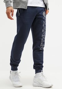 Marinblå sweatpants med vit "FRANKLIN" text tryckt vertikalt på vänster ben, med resårmidja och muddar.