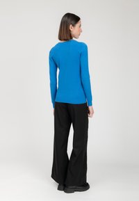 Suéter azul de punto con mangas largas y cuello redondo, combinado con pantalones amplios negros y calzado negro grueso.