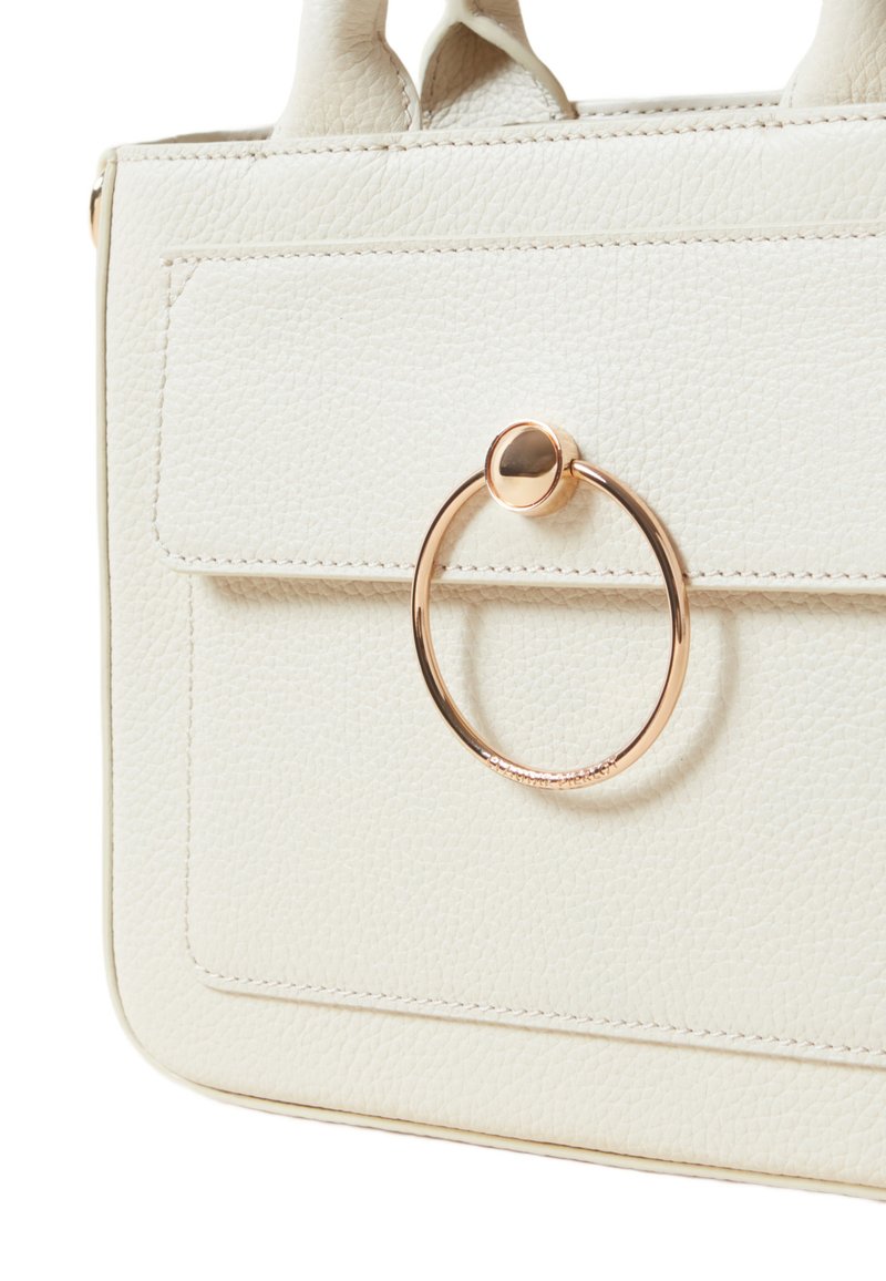 Sac à main en faux cuir crème avec une surface texturée, de forme rectangulaire, des poignées supérieures et un accent matériel doré circulaire sur le devant.