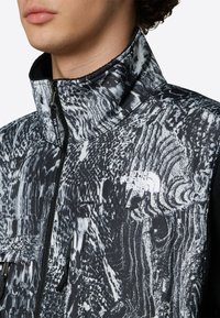 Czarna i biała kamizelka bez rękawów w wzory, z wysokim kołnierzem, zamkiem błyskawicznym i logo The North Face na klatce piersiowej. Teksturowany materiał.