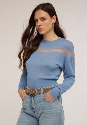 Pull en maille bleu clair avec un col rond, des manches longues et une rayure transparente sur la poitrine. Associé à un jean taille haute et une ceinture marron.