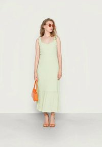 Vestido midi verde claro com alças com folhos, tecido texturizado e bainha rodada, combinado com uma bolsa laranja e sandálias de salto bloco castanhas.