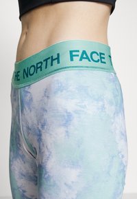 Ljusblå leggings med marmormönster, med en bred teal midja och "THE NORTH FACE"-logotyp i mörk teal. Slät textur.