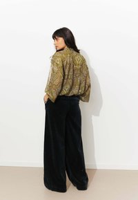 Blouse ample avec un motif paisley en vert olive et blanc, associé à un pantalon large en velours côtelé noir. Texture lisse.