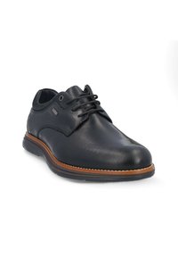 Zapato de vestir de cuero negro con superficie texturizada, punta redonda, diseño con cordones y detalle de suela marrón contrastante.