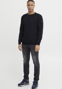 Svart strikkegenser med rund hals, ribbede mansjetter og kant, sammen med mørk grå jeans og blå sneakers. Minimalistisk design.