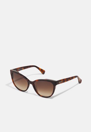 Gafas de sol de carey con forma de ojo de gato, lentes marrones degradados, montura gruesa y detalles de logo sutiles en las patillas.