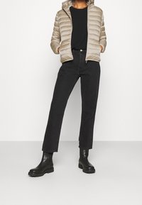 Beige puffatakki hupparilla, tikattu malli. Musta pitkähiha shirtti, suorat mustat farkut ja mustat paksupohjaiset nilkkurit.