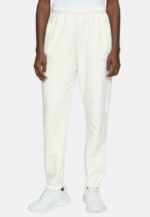 Weiße Sweatpants mit elastischem Bund und Bündchen, ausgestattet mit seitlichen Taschen und einem dezenten Logodetail auf der Vorderseite. Kombiniert mit weißen Turnschuhen.