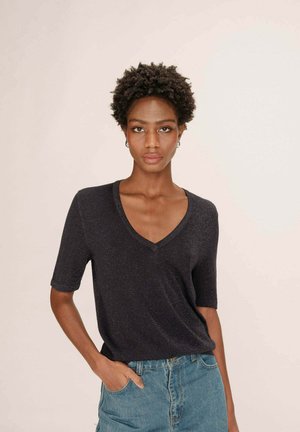 T-shirt bleu marine à col en V et manches courtes, fabriqué à partir d'un tissu texturé. Associé à un jean en denim bleu clair, légèrement rentré à l'avant.