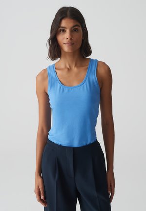 Blue cotton tank top with a scoop neckline, fitted design, and smooth texture, paired with dark tailored pants.