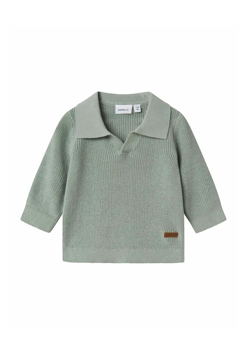 Maglione lavorato a maglia verde chiaro con ampio colletto e maniche a tre quarti. Presenta un'etichetta di accento marrone sul lato inferiore.