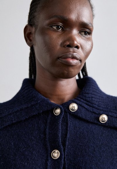 Navy wool cardigan with a structured collar, featuring silver-tone buttons and a textured knit pattern. Close-up view emphasizes details.