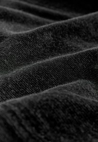 Gros plan d'un tissu noir doux avec une texture tricotée visible et des plis doux créant des vagues ombrées à la surface.