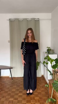 Black off-shoulder jumpsuit with a gathered waist, featuring wide leg trousers. Accessorized with a black-and-white polka dot bag strap.