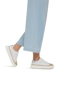Sneakers bianchi con una punta strutturata beige e accenti argentati, caratterizzati da una suola spessa e rigata e lacci, abbinati a pantaloni a gamba larga blu chiaro.