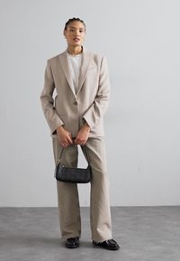 Beiger, übergroßer Blazer, weißes T-Shirt, hellgraue, weit geschnittene Hose, schwarze Handtasche und schwarze Schuhe; glatte Textur und taillierte Passform.