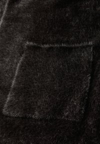 Svart päls tyg med en mjuk textur, med en fickdetalj. Ytan är tät och fluffig, vilket skapar ett mysigt utseende.