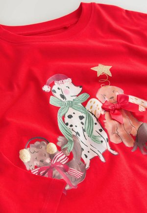 Röd t-shirt med illustrationer av hundar i festkläder. Inkluderar en dalmatiner, en brun hund med öronmuffar och en tredje hund med änglavingar och rosetter.