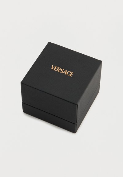 Fekete négyzet alakú ékszerdoboz arany "VERSACE" logóval középen a tetején, egyszerű fehér háttér előtt.