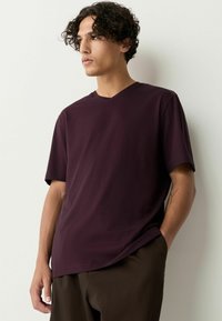 V-ringad, kortärmad t-shirt i djup vinröd bomullstyg. Avslappnad passform med en mjuk textur. Bärs med mörkbruna byxor.