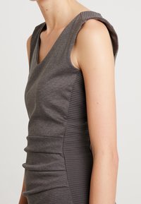 Robe grise sans manches avec un col en V, dotée d'accents côtelés aux épaules et de fronces sur les côtés pour une silhouette ajustée.